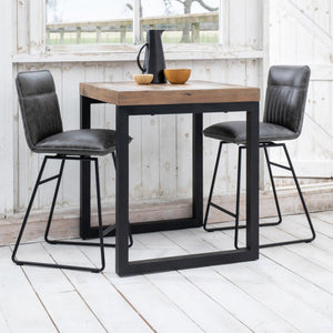 Wooden dining table with black metal legs and two matching chairs on a white wooden floor.