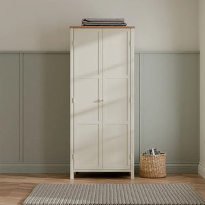 White wardrobe with two doors in a room with green walls and a woven basket on the floor.