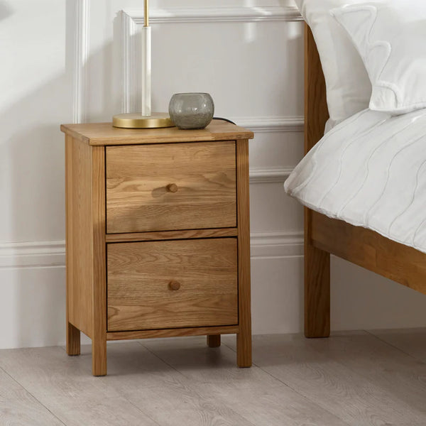 Wooden nightstand with two drawers next to a bed in a bedroom setting.
