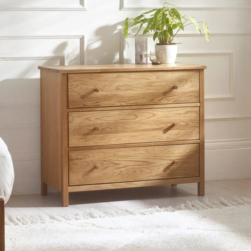 A three drawer chest in oak on a white background