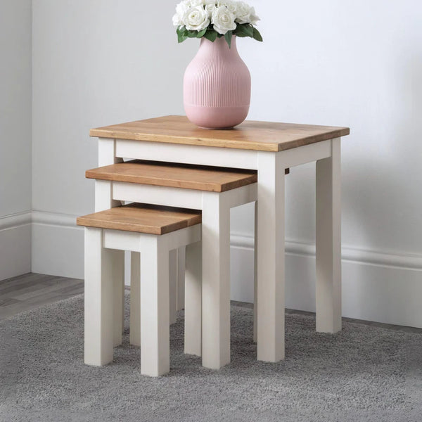 Set of three nesting tables with a pink vase and white flowers on top against a plain wall.