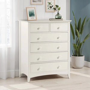 White dresser with decorative items in a room with a plant and framed pictures.