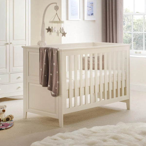 White crib in a nursery with a starry blanket and toys.