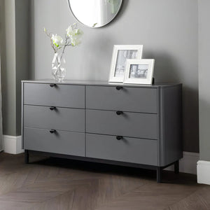 Gray dresser with black handles in a room with a mirror and framed pictures.