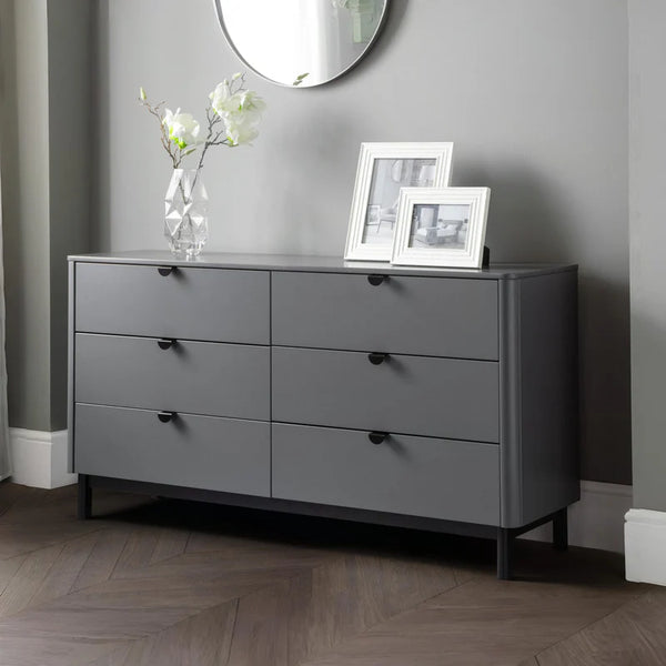 Gray dresser with black handles in a room with a mirror and framed pictures.