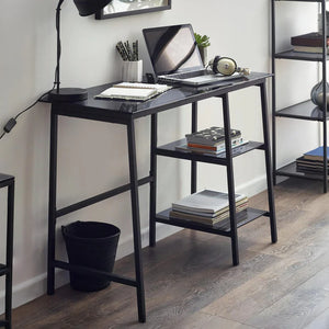 Black desk with laptop, books, and stationery in a home office setting.