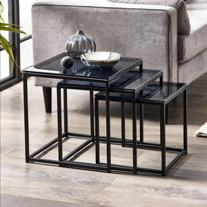 Set of black nesting tables with decorative items on a wooden floor.