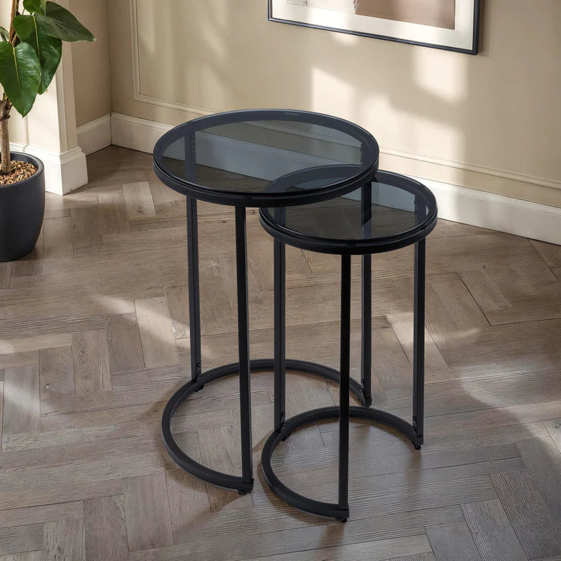 Set of two black metal nesting tables with glass tops on a white background