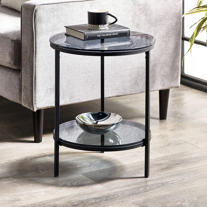 Round side table with glass top and black metal frame on a white background