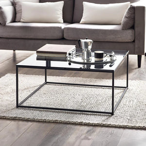 Modern living room with a glass coffee table, books, and a teapot.