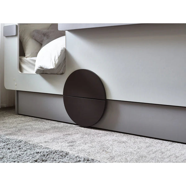 Modern bed with white frame and dark circular footboard on a carpeted floor.