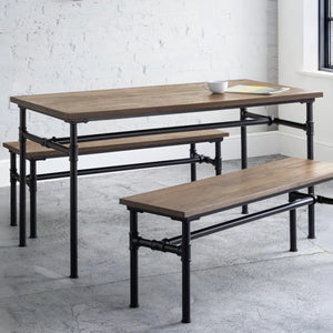 Wooden dining table with benches on a concrete floor against a white brick wall.