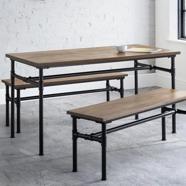 Wooden dining table with benches on a concrete floor against a white brick wall.