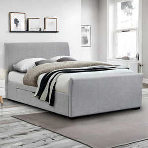 Gray upholstered bed in a room with framed pictures on the wall.