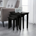 Set of black nesting tables in a living room setting with a sofa and curtains.