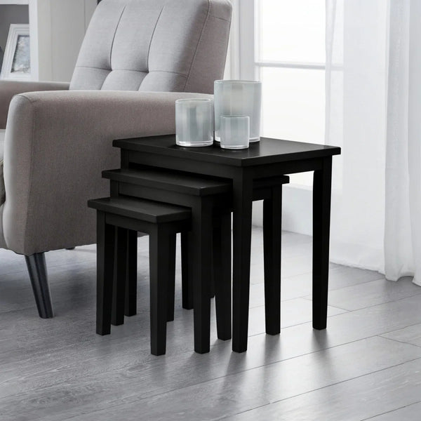 Set of black nesting tables in a living room setting with a sofa and curtains.