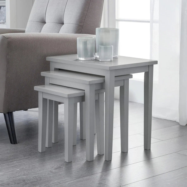 Set of three gray nesting tables with glass candle holders in a living room setting.