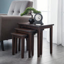 Set of four dark wood nesting tables in a living room setting with a chair and decorative items.