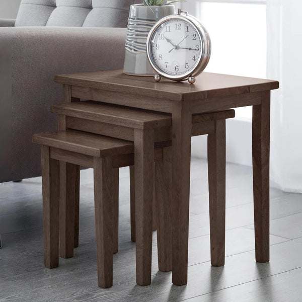 Set of three wooden nesting tables with a clock on top in a living room setting.