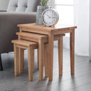 Set of three wooden nesting tables with a clock on top in a living room setting.