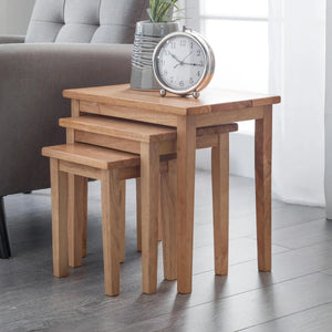 Set of three wooden nesting tables with a clock on top in a living room setting.