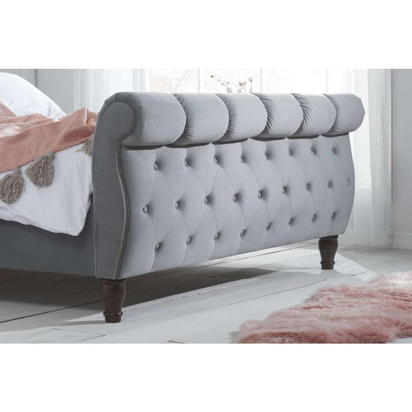 Gray tufted bed with wooden legs in a bedroom setting