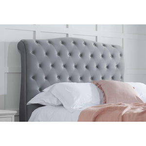 Gray tufted headboard with pillows and a blanket against a white paneled wall.