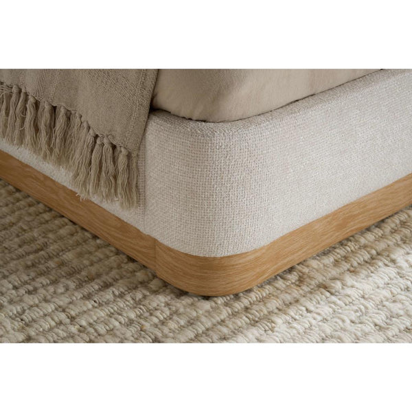 Corner of bed frame upholstered in a textured fabric with a wood surround