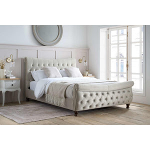 Beige upholstered bed in a bright bedroom with large windows.