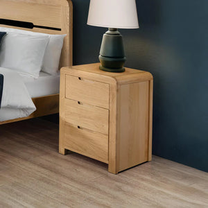 Wooden nightstand with a lamp next to a bed in a bedroom setting.