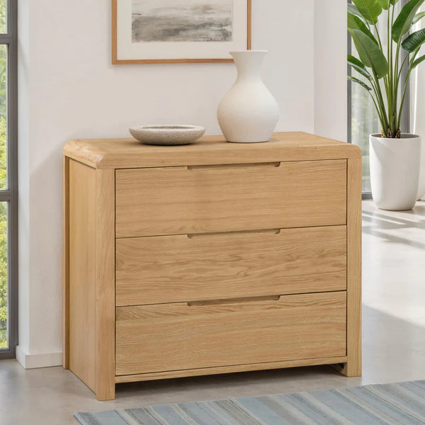 Wooden dresser with three drawers in a room with a plant and framed picture.
