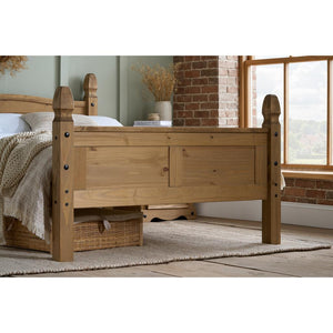 Wooden bed in a room with a window and brick wall.
