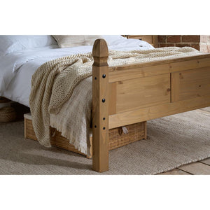 Wooden bed with a textured blanket on a carpeted floor