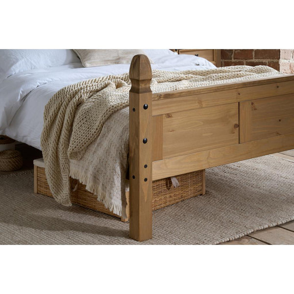 Wooden bed with a textured blanket on a carpeted floor
