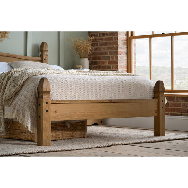 Wooden bed with white bedding in a room with a window and brick wall.