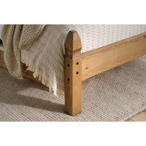 Wooden bed frame with a textured blanket on a carpeted floor