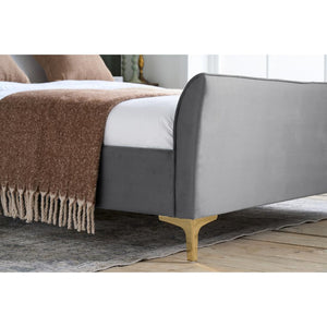 Gray upholstered bed with a brown blanket on a wooden floor.