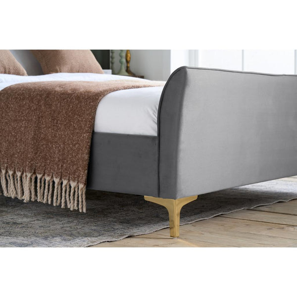 Gray upholstered bed with a brown blanket on a wooden floor.