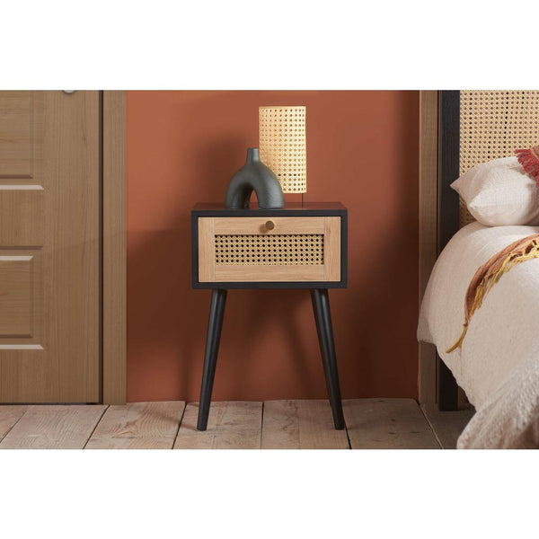 Bedside table with woven design and lamp against a warm-colored wall.