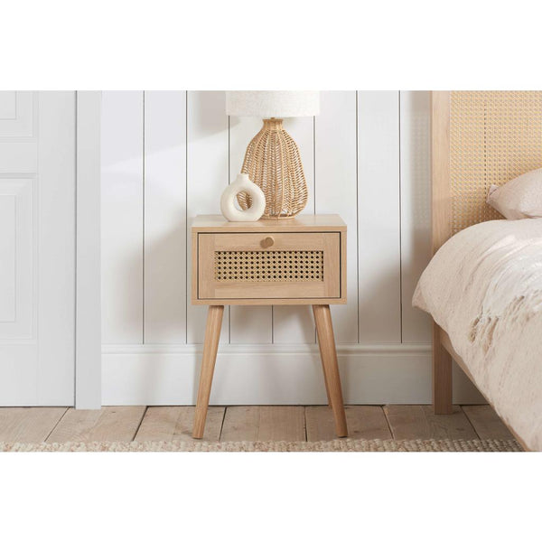 Wooden bedside table with decorative items next to a bed with a woven headboard.