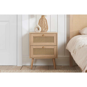 Wooden nightstand with wicker design against a white wall in a bedroom setting.