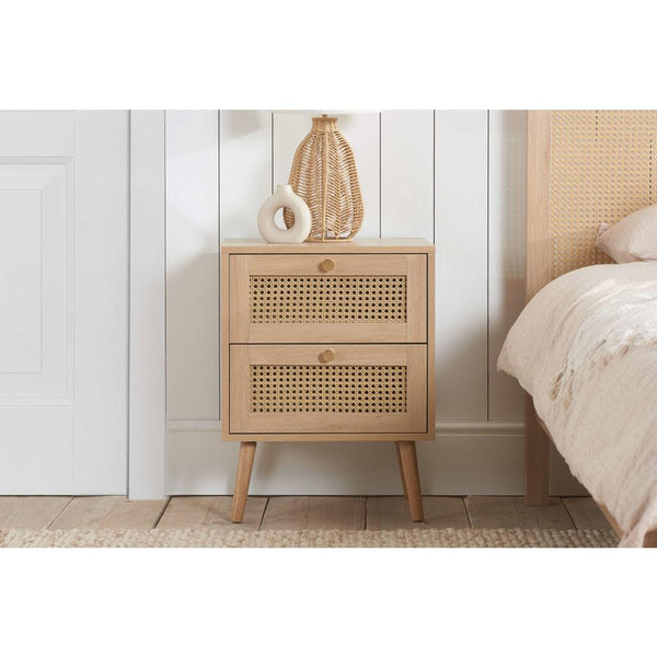 Wooden nightstand with wicker design against a white wall in a bedroom setting.
