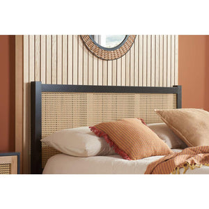 Bed with rattan headboard and pillows against a striped wall.