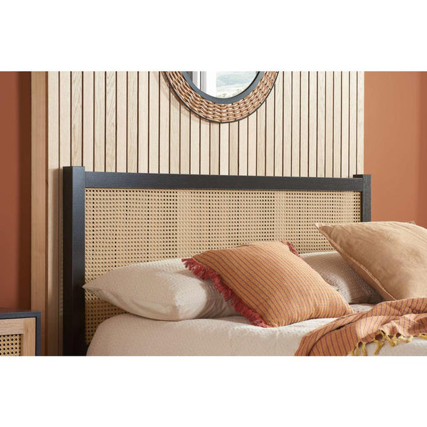 Bed with rattan headboard and pillows against a striped wall.