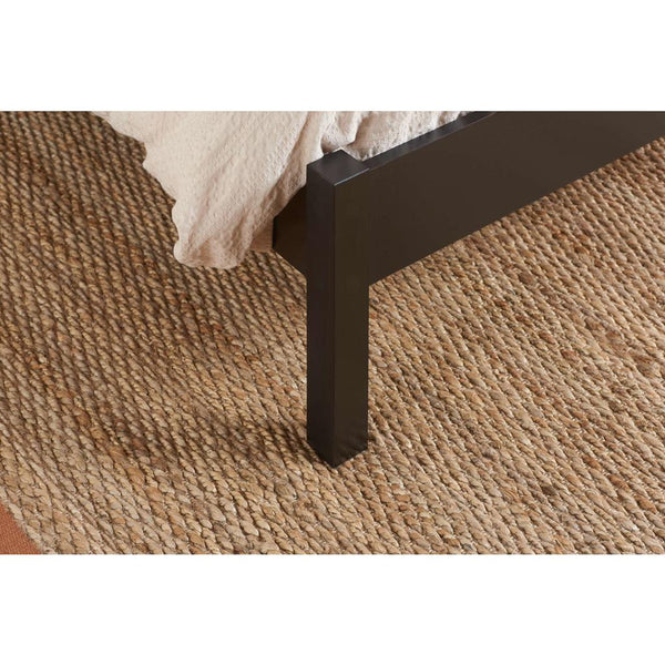 Close-up of a black bed frame corner on a textured brown carpet