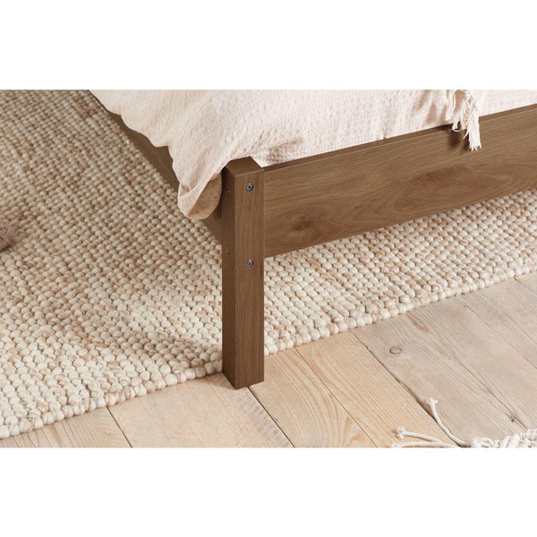 Wooden bed frame on a textured rug with a neutral color scheme