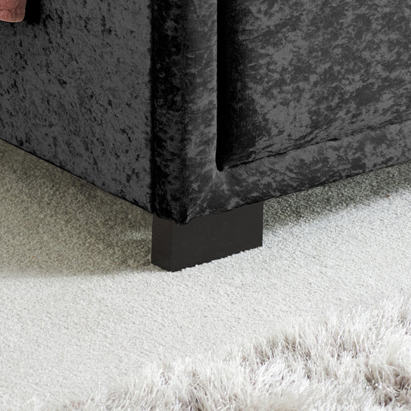 Close-up of a black velvet bed with a black foot on a carpeted floor.
