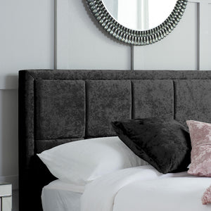 Black upholstered headboard with pillows on a bed against a white wall with a decorative mirror.