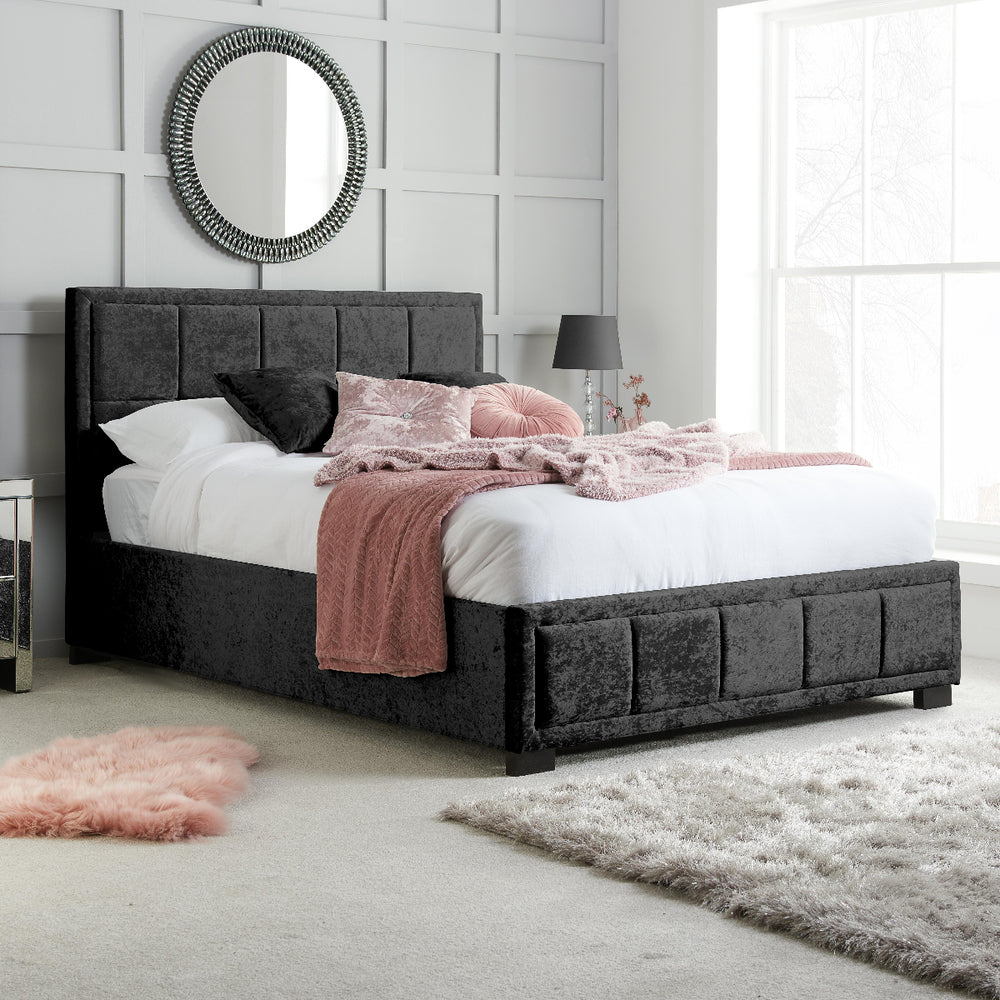 Black upholstered bed with bedding on a white background