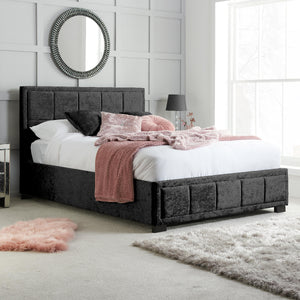 Black upholstered bed in a bedroom with white walls and a mirror.